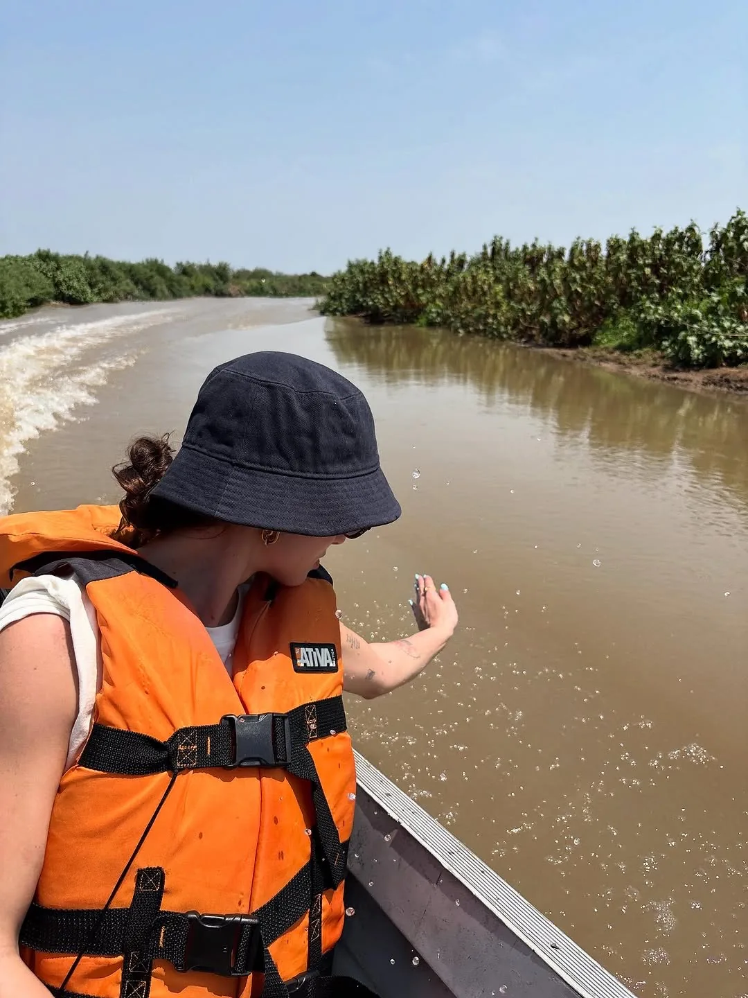 Participante de colete laranja tocando a água durante navegação pelo rio Cuiabá