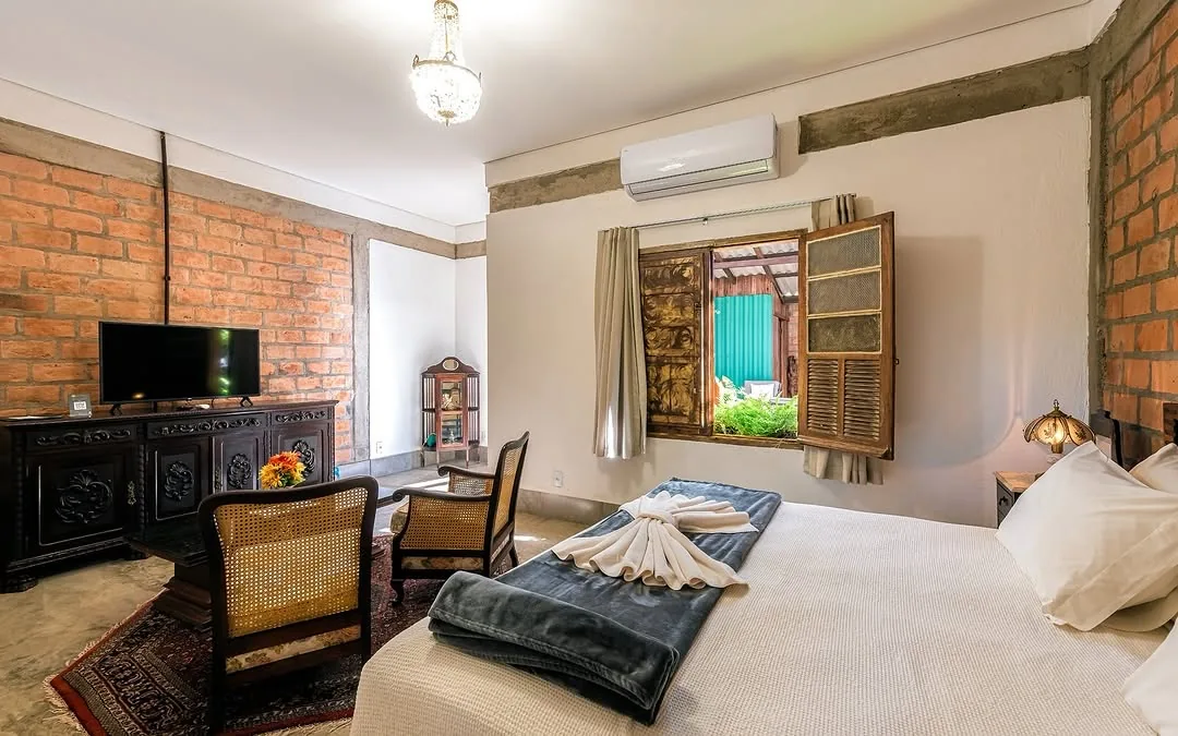 Interior da suíte da pousada com cama, móveis vintage e iluminação acolhedora